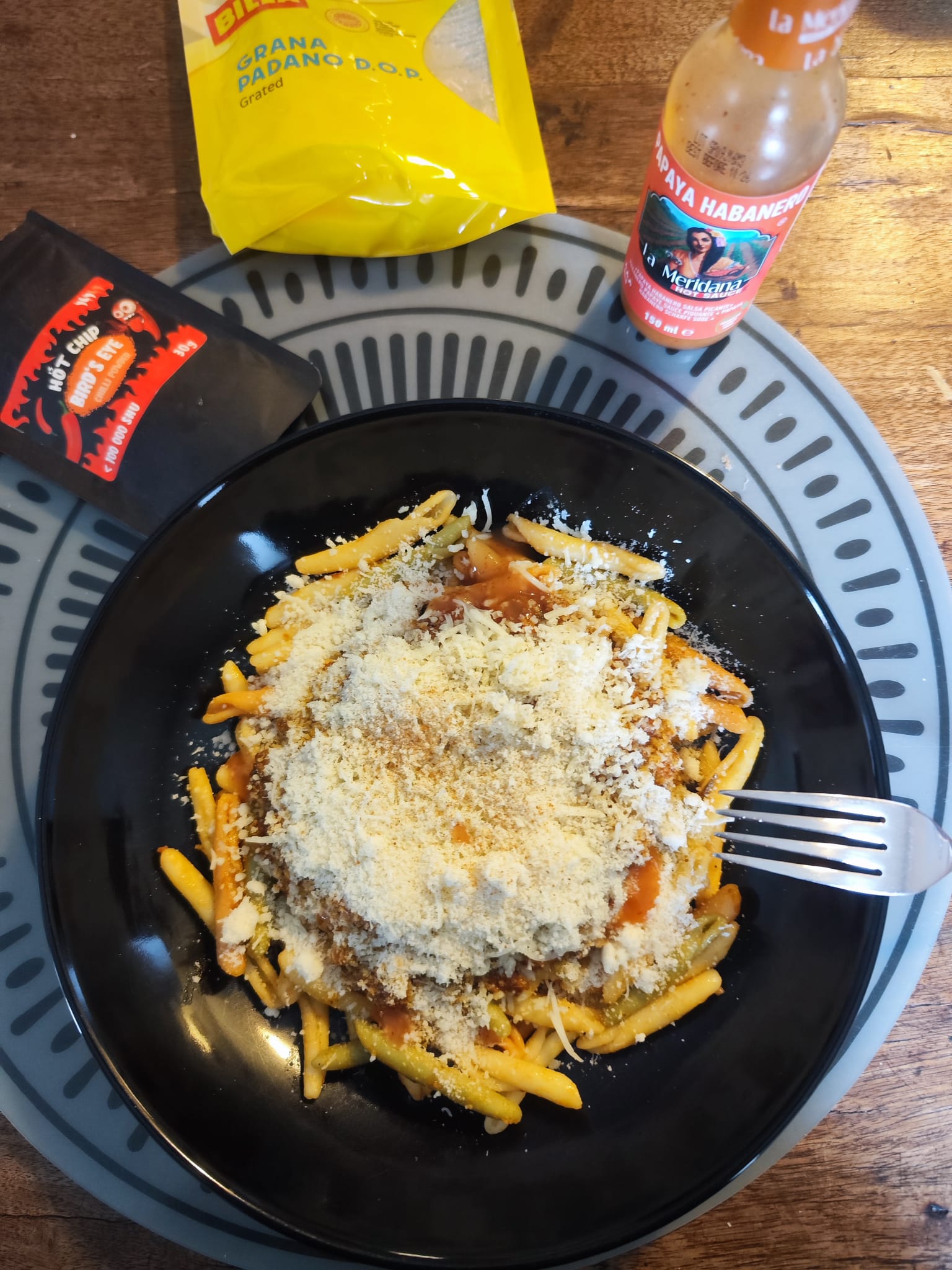 The finished bowl — buried under Grana Padano, hot sauce on standby